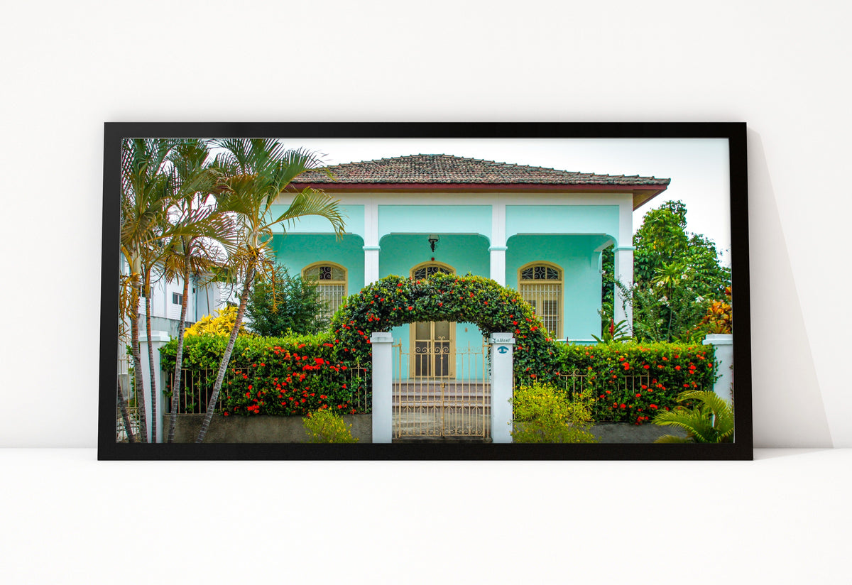 Poster Cuba Villa 5 ingelijst, kleurenfoto van een mintgroene villa met een poort van rode bloemen en hoge palmen ernaast