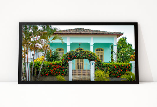 Poster Cuba Villa 5 ingelijst, kleurenfoto van een mintgroene villa met een poort van rode bloemen en hoge palmen ernaast