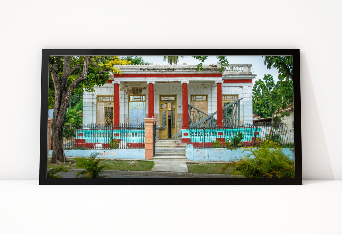 Poster Cuba Villa 6 ingelijst, kleurenfoto van een villa met rode zuilen, gele deuren en een turquoise hek langs de straat
